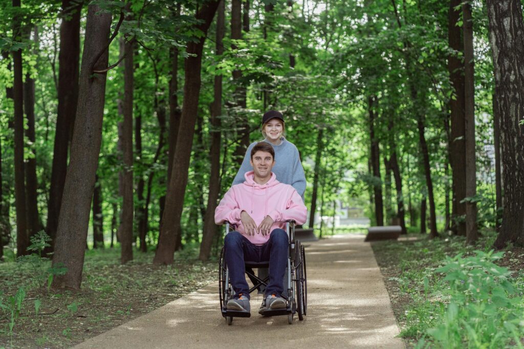 Smiling couple enjoying a sunny day in a park. Man in a wheelchair being pushed by a woman.
